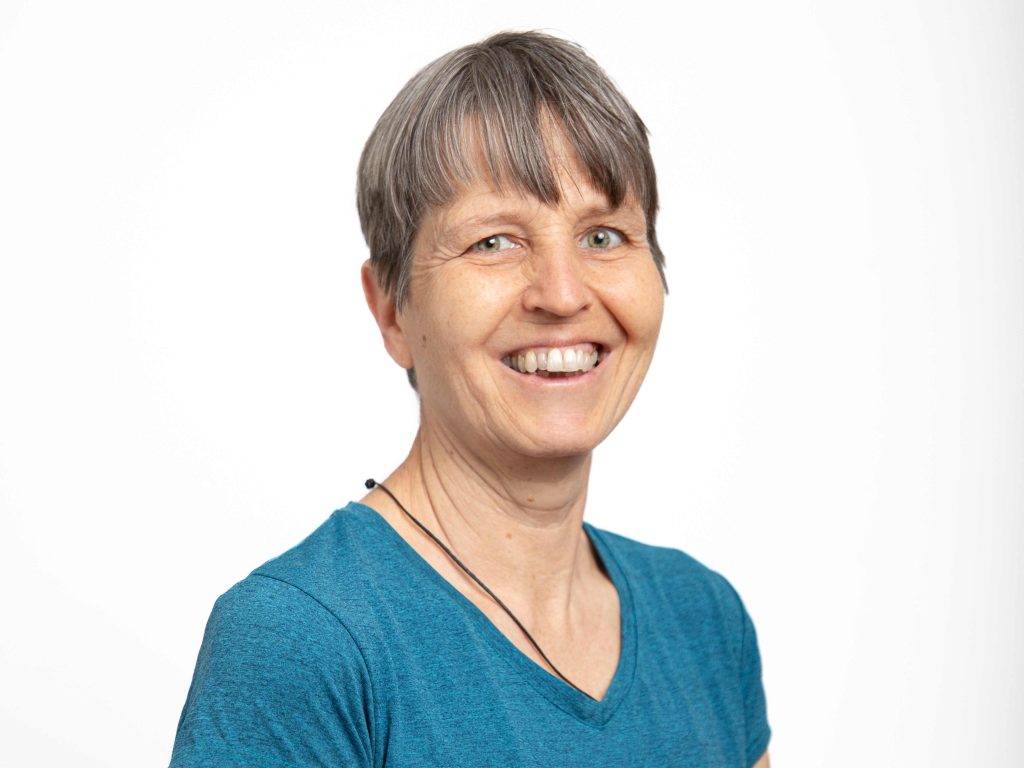 Frau mit kurzem Haar und blauem T-Shirt lächelt in die Kamera.